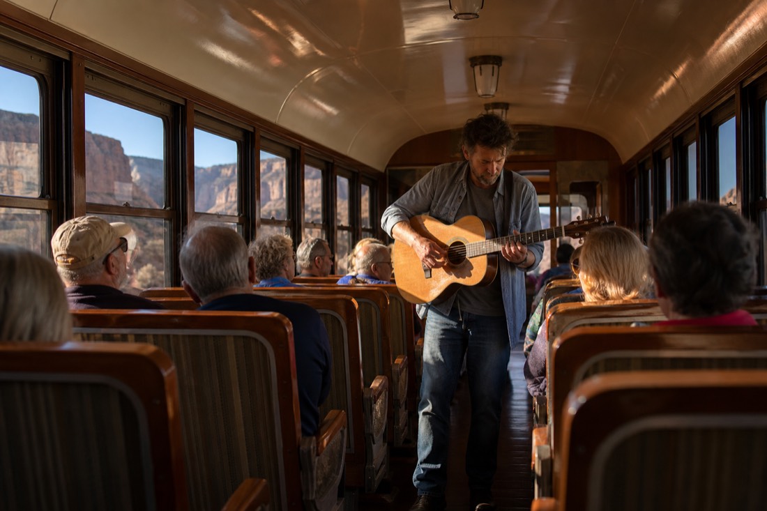 A musician with a guitar entertaining passengers in the aisle of a restored railway car