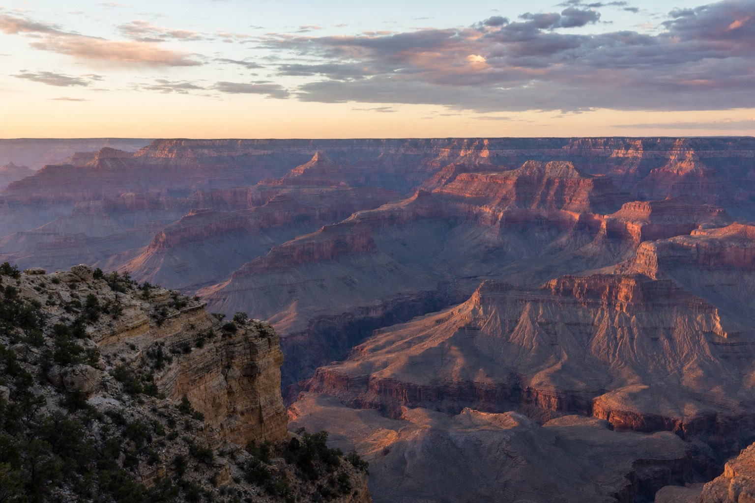 Vast roadless expanse of the Grand Canyon stretching to the horizon beyond a lone rim viewpoint at dusk