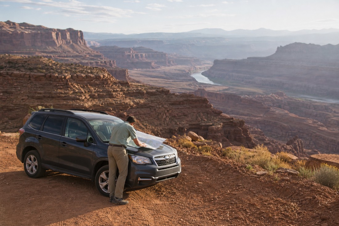 A rental SUV parked at a desert overlook with the driver checking a road map on the hood