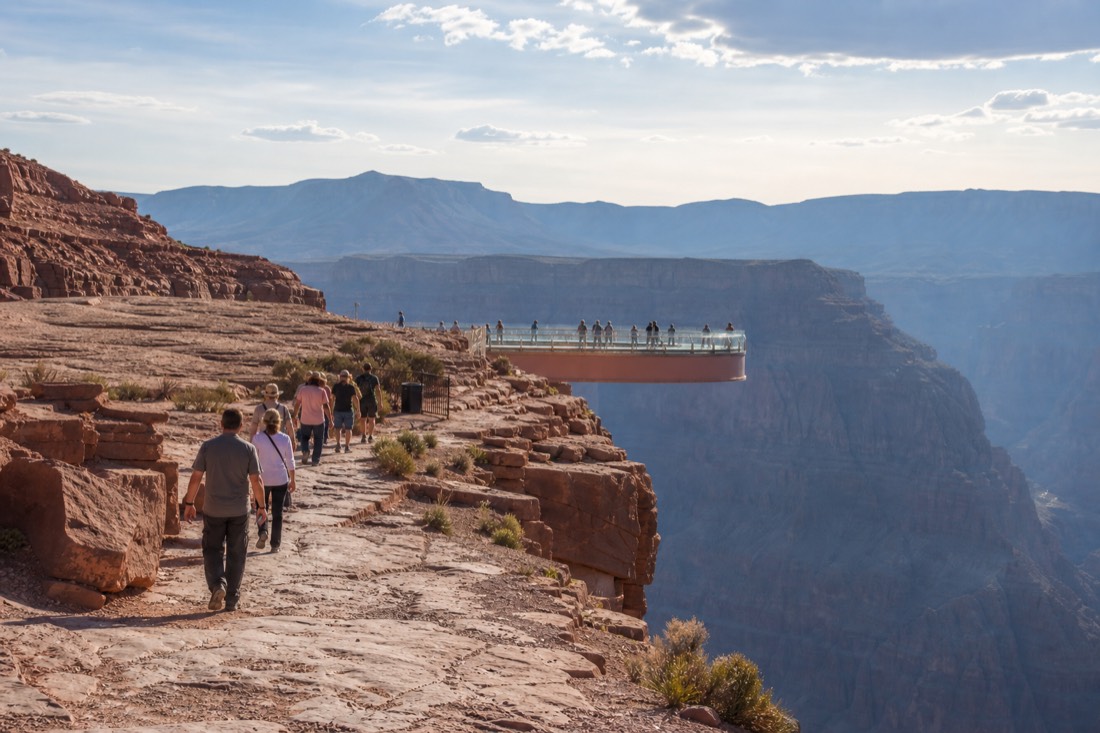 Visitors walking toward the horseshoe-shaped glass Skywalk bridge at Grand Canyon West under desert sun
